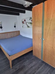 Ein gemütliches Schlafzimmer mit einem Holzbetten und einem großen Kleiderschrank. Die Wände sind hell gestrichen und es gibt eine stilvolle Wanddekoration.