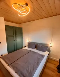 Ein gemütliches Schlafzimmer mit einem Doppelbett und modernen Lampen. Die Wände sind hell und es gibt einen Kleiderschrank in einem dunklen Grünton.