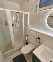 Ein modernes Badezimmer mit einer Dusche, einem Waschbecken und einem WC. Die Wände sind fliesenverkleidet und es gibt eine große Spiegelbeleuchtung.