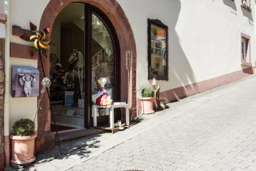 Ein charmantes Geschäft mit einem runden Eingang. Vor dem Laden stehen Blumentöpfe und bunte Dekorationen.