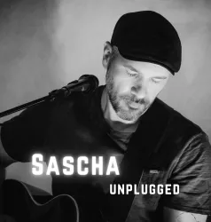 Ein Musiker spielt Gitarre und singt in einem gemütlichen Setting. Der Fokus liegt auf seiner emotionalen Darbietung.