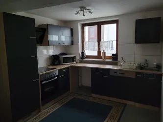 Eine moderne Küche mit dunklen Schränken und einer hellen Arbeitsfläche. Es gibt Geräte wie einen Herd, einen Kühlschrank und eine Mikrowelle.