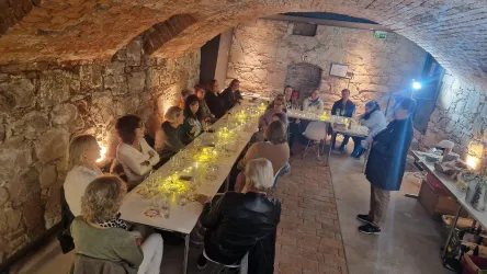 Eine Gruppe von Menschen sitzt an langen Tischen in einem historischen Keller. Der Raum hat sichtbare Steinwände und eine gemütliche Beleuchtung.