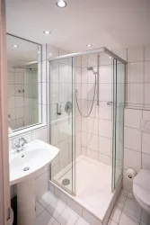 Ein modernes Badezimmer mit einer Glaskabine für die Dusche. Der Raum ist hell und mit weißen Fliesen gefliest.