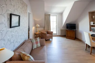 Ein helles Wohnzimmer mit einem Sofa und zwei bequemen Sesseln. Ein Fernseher und ein Schreibtisch sind ebenfalls im Raum vorhanden.