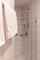 Ein modernes Badezimmer mit einer Dusche und weißen Handtüchern. Die Wände sind gefliest und die Ausstattung ist schlicht und funktional.
