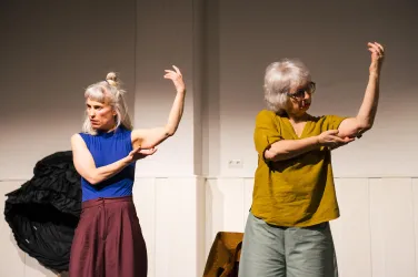 Zwei Frauen führen eine künstlerische Bewegung darstellende Performance auf. Sie stehen in einem hellen Raum und zeigen mit ihren Armen verschiedene Posen.