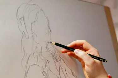 Eine Hand zeichnet eine Skizze auf einer Leinwand. Der Stil ist einfach und zeigt eine Person.