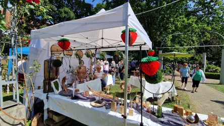 Ein Marktstand mit künstlerischen Handwerken und Dekorationen unter einem weißen Zelt. Im Hintergrund sind Menschen zu sehen, die die Umgebung erkunden.