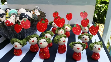 Eine Gruppe von handgemachten Figuren in Erdbeerwindeln steht auf einem Tisch. Im Hintergrund sind weitere dekorierte Figuren in einer Schüssel.