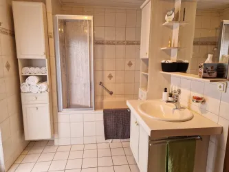 Ein Badezimmer mit einer Duschbadewanne, einem Waschbecken und Handtüchern/Badetüchern. Die Einrichtung ist hell und freundlich gestaltet.