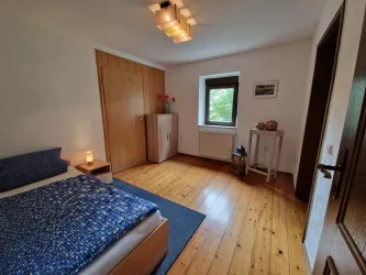 Ein gemütliches Schlafzimmer mit einem Bett und einem hellen Holzfußboden. Das Zimmer hat ein Fenster, das viel Tageslicht hereinlässt.