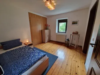 Ein gemütliches Schlafzimmer mit Holzfußboden und einem Einzelbett. Das Zimmer hat einen Schrank und ein Fenster mit Blick ins Grüne.