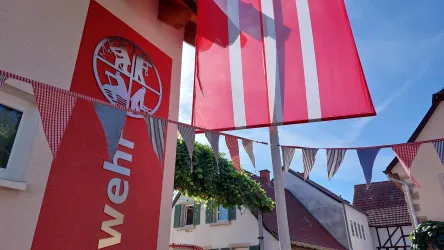 Ein Gebäude mit einer großen roten Fahne und einem Wappen. Bunte Wimpel sind entlang der Fassade aufgehängt.