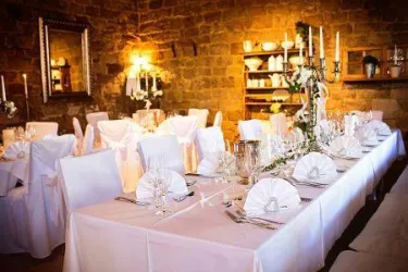 Ein elegant gedeckter Tisch in einem gemütlichen Raum. Die Tische sind mit weißen Tischtüchern und dekorativen Servietten eingedeckt, umgeben von warmem Licht.