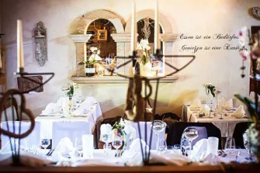 Ein elegantes Restaurant mit schön gedeckten Tischen und Kerzenlicht. An der Wand hängt ein Spruch, der die Atmosphäre unterstreicht.