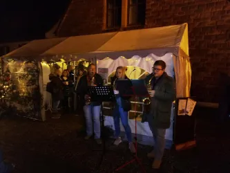 Eine Weihnachtsveranstaltung mit Musikern, die Saxophon spielen. Im Hintergrund ist ein beleuchteter Festzelt und Zuschauer sind zu sehen.