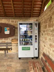 Ein Automat mit regionalen Produkten steht in einem überdachten Bereich. Er enthält verschiedene Flaschen und Dosen.