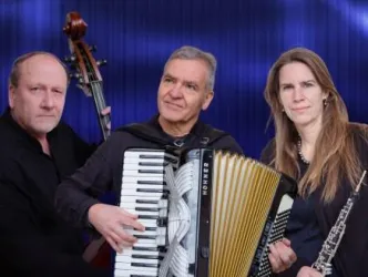 Drei Musiker stehen zusammen und spielen verschiedene Instrumente. Im Vordergrund sind ein Akkordeonspieler und eine Frau mit einer Querflöte, während ein Doppelbassist im Hintergrund steht.