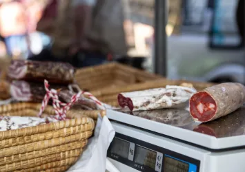 Ein Marktstand mit verschiedenen Wurstsorten. Im Vordergrund liegt eine Wurst auf einer Waage.