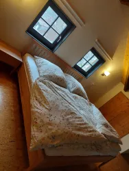 Ein gemütliches Schlafzimmer mit einem Holzbett und bunten Bettdecken. Zwei Fenster lassen natürliches Licht herein.