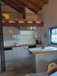 Eine moderne Küche mit Holzregalen und einem offenen Obergeschoss. Die Wände sind hell und es gibt einen kleinen Tisch mit Blumen auf der Arbeitsfläche.