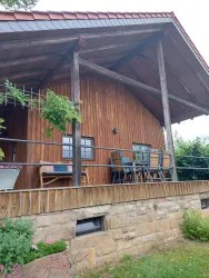 Ein Holzhaus mit einem überdachten Balkon und einer schönen Veranda. Auf der Veranda stehen Gartenmöbel und es gibt Pflanzen im Vordergrund.