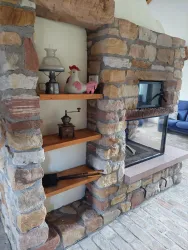 Ein rustikaler Kamin aus Stein mit Holzregalen. Auf den Regalen sind dekorative Gegenstände und eine warmherzige Atmosphäre zu sehen.