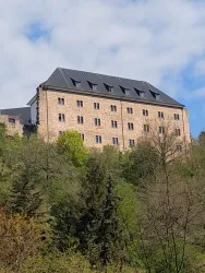 Ein altes Gebäude auf einem Hügel, umgeben von Bäumen und Grün. Der Himmel ist teilweise bewölkt und vermittelt eine ruhige Atmosphäre.
