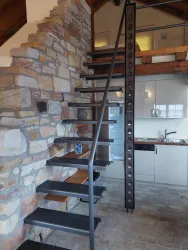 Eine moderne Treppe aus Metall und Holz in einem rustikalen Raum. Die Wand ist mit natürlichem Stein verkleidet, und es gibt eine offene Küchenzeile im Hintergrund.