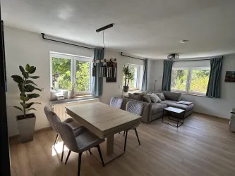 Ein helle und moderne Wohnküche mit einem Esstisch und gemütlicher Couch. Große Fenster lassen viel Licht herein und schaffen eine freundliche Atmosphäre.