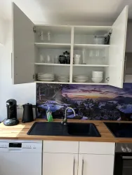 Eine moderne Küche mit einem Holzarbeitsplatz und weißen Schränken. Im Hintergrund ist ein malerisches Wandbild einer Landschaft zu sehen.