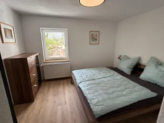 Ein gemütliches Schlafzimmer mit einem Doppelbett und hellen Bettdecken. Ein Fenster und eine Kommode sorgen für eine freundliche Atmosphäre.