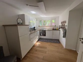 Eine moderne Küche mit weißen Schränken und Holzfußboden. Licht fällt durch die Fenster und schafft eine helle, einladende Atmosphäre.