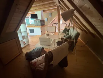 Ein gemütlicher Wohnraum im Dachgeschoss mit modernen Möbeln. Der Raum ist hell und einladend, mit Holzverkleidung und einem kleinen Essbereich.