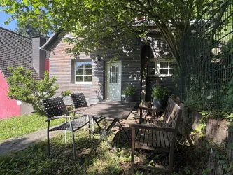 Ein gemütlicher Garten mit einem Tisch und Stühlen vor einem kleinen Haus. Die Umgebung ist grün und einladend, ideal für entspannte Stunden im Freien.