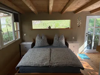 Ein gemütliches Schlafzimmer mit einem großen Doppelbett und zwei Nachttischen. Das Fenster bietet einen Blick ins Grüne und lässt viel Tageslicht herein.