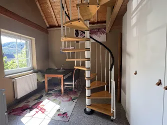 Eine helle und einladende Innenansicht mit einer Wendeltreppe und einem Tisch. Große Fenster lassen viel Tageslicht herein.