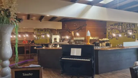 Eine gemütliche Außenterrasse eines Restaurants mit Gästen, die Getränke genießen. Sonnenschein und schattenspendende Schirme schaffen eine einladende Atmosphäre.