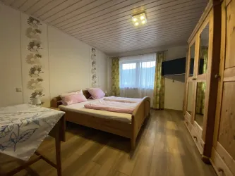 Ein gemütliches Schlafzimmer mit einem Doppelbett und bunten Vorhängen. Es gibt einen Tisch sowie einen Schrank und einen Fernseher an der Wand.