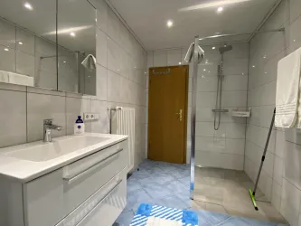 Ein modernes Badezimmer mit hellen Fliesen und einer Duschkabine. Es gibt einen Waschbecken mit Spiegel und einen Handtuchhalter.