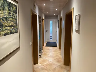 Ein heller Flur mit mehreren Türen und einer Aussicht auf den Eingang. An der Wand hängt ein Bild, und die Bodenfliesen sind hell und gepflegt.