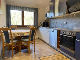 Eine moderne Küche mit einem runden Esstisch und vier Stühlen. Im Hintergrund sind Fenster und Küchenschränke zu sehen.