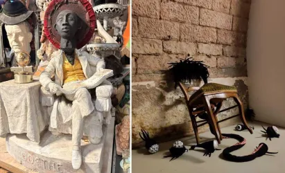 Eine stilisierte Statue einer sitzenden Person mit einem sonnigen Hut und bunter Kleidung. Daneben liegen unheimliche, kreative Objekte auf dem Boden, inklusive einer umgedrehten Stuhl.