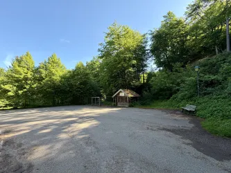 Ein ruhiger Parkplatz umgeben von grünen Bäumen. In der Nähe steht ein kleines Häuschen und eine Bank zum Entspannen.
