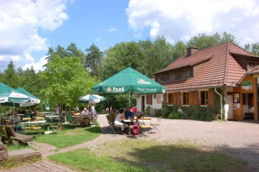 Ein gemütliches Restaurant mit einer Terrasse im Freien. Grüne Bäume und Sonnenschirme schaffen eine einladende Atmosphäre.