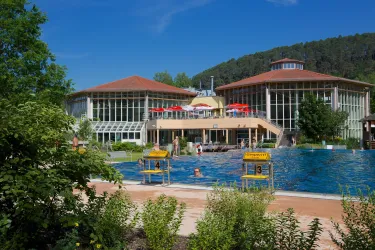 Ein Schwimmbad mit klarem Wasser und einer modernen Architektur. Umgeben von Bäumen und einem sonnigen Himmel.