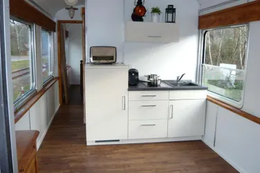 Eine moderne Küche in einem hellen Raum mit Holzverkleidung. Sie verfügt über eine Spüle, Kochutensilien und große Fenster, die viel Licht hereinlassen.