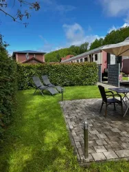 Ein gepflegter Garten mit Rasen und gepflasterter Terrasse. Zwei Liegen und ein Tisch mit Stühlen laden zum Entspannen ein.