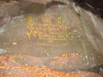 Ein Fels mit einer in gelber Farbe geschriebenen Inschrift aus dem Jahr 1928. Die Gravur enthält Namen und ein dekoratives Muster.